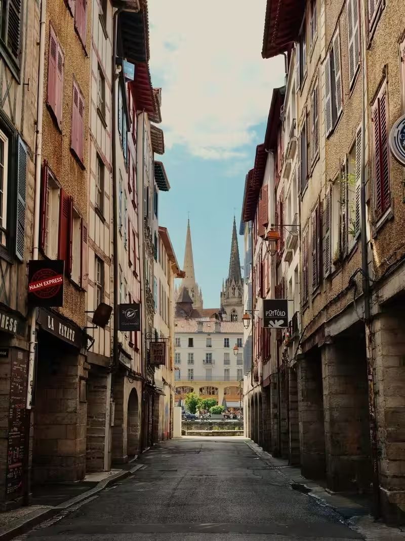 Une rue étroite de la vieille ville de Bayonne, façades à colombages et arcades de pierre, les deux flèches de la cathédrale au fond