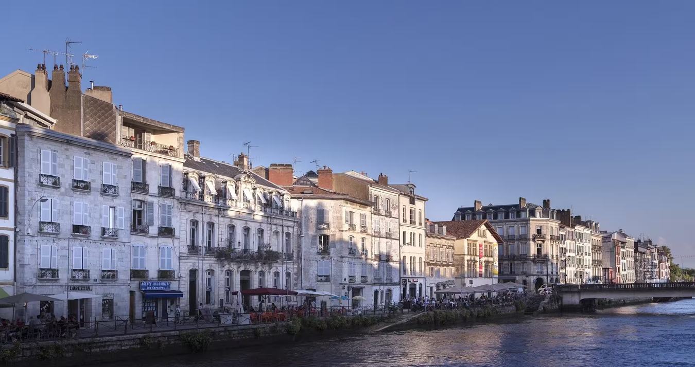 Les quais de la Nive à Bayonne au soleil couchant, les façades à volets et arcades alignées le long de l'eau, et le pont Marengo au fond
