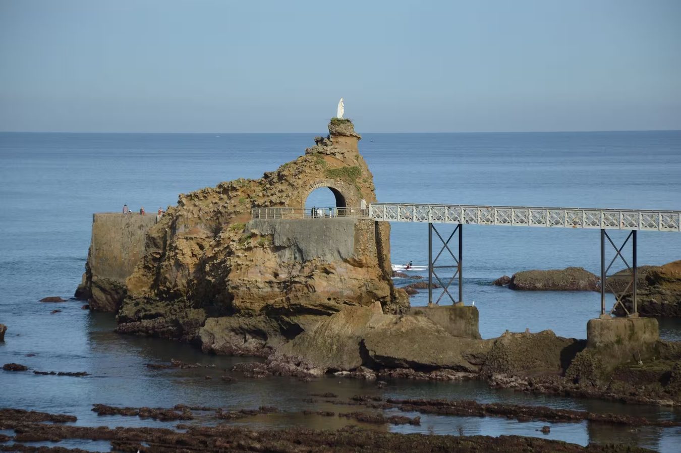 Le rocher de la Vierge à Biarritz, la statue blanche à son sommet et la passerelle métallique qui le relie à la côte, l'océan calme et bleu derrière