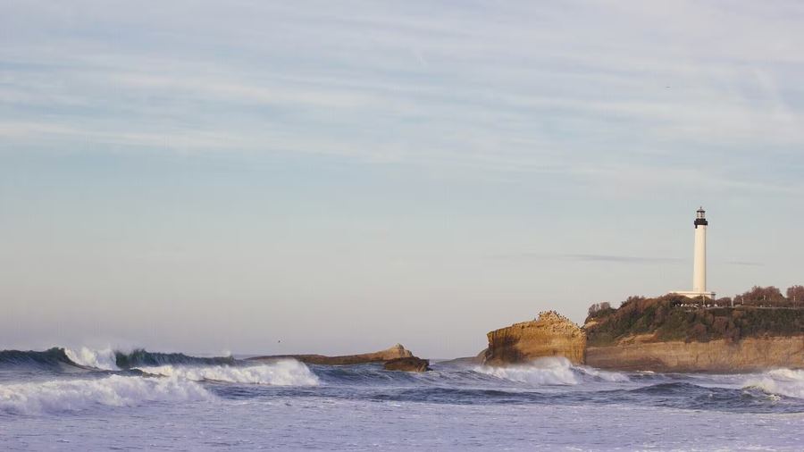 Le phare de Biarritz au sommet de sa falaise, les rouleaux de l'océan se brisant en contrebas dans la lumière du soir