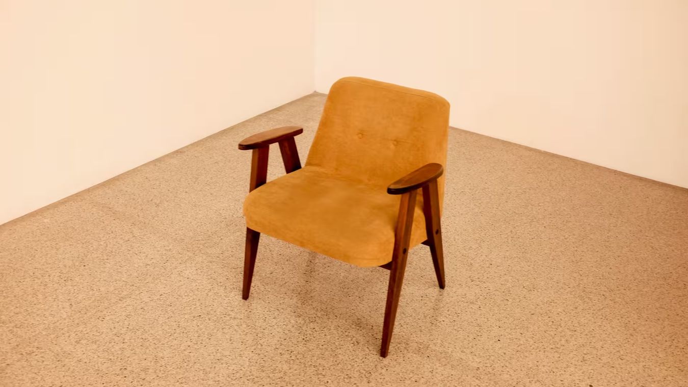 Un fauteuil en tissu ocre aux accoudoirs de bois, seul dans une pièce claire
