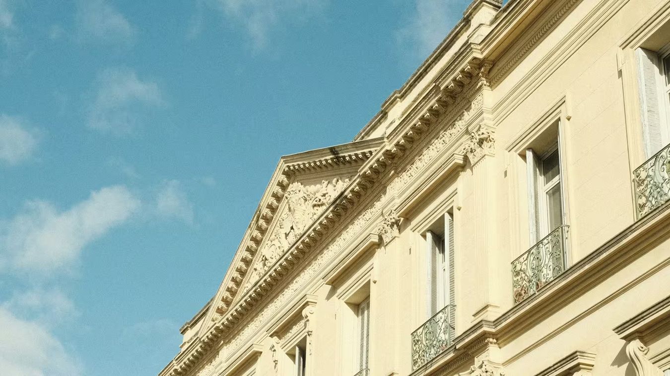 Une façade de pierre claire aux hautes fenêtres et balcons en fer forgé, sous un ciel bleu